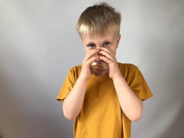 petit garçon dans un t-shirt jaune boit de l'eau