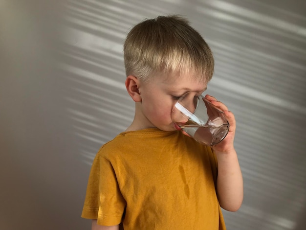 petit garçon dans un t-shirt jaune boit de l'eau