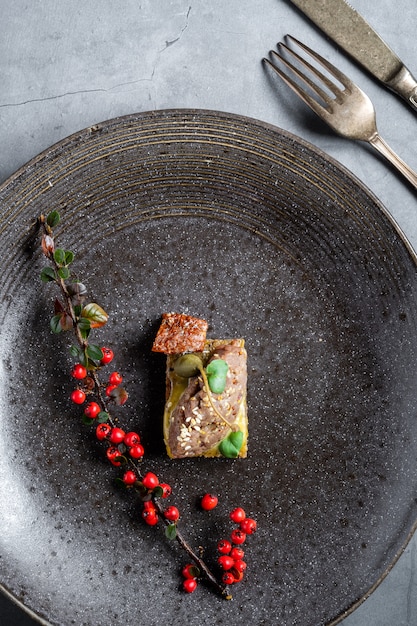 Photo petit sandwich à tapas sur un plus grand plat sombre sur un fond de table en béton. décoré d'une brindille aux fruits rouges et d'une fourchette avec un couteau.