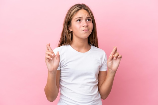 Petite fille caucasienne isolée sur fond rose avec les doigts croisés et souhaitant le meilleur