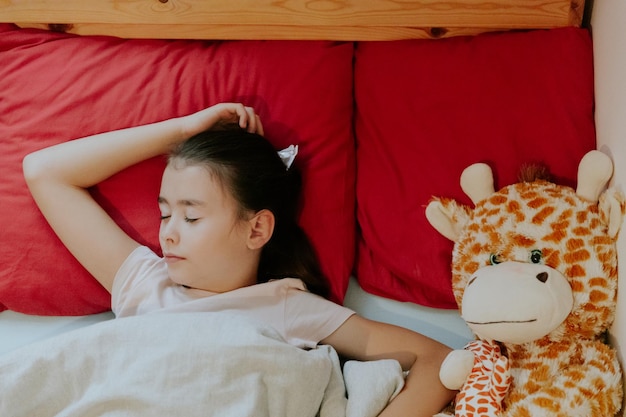 Photo une petite fille dort dans un lit avec un jouet de girafe.