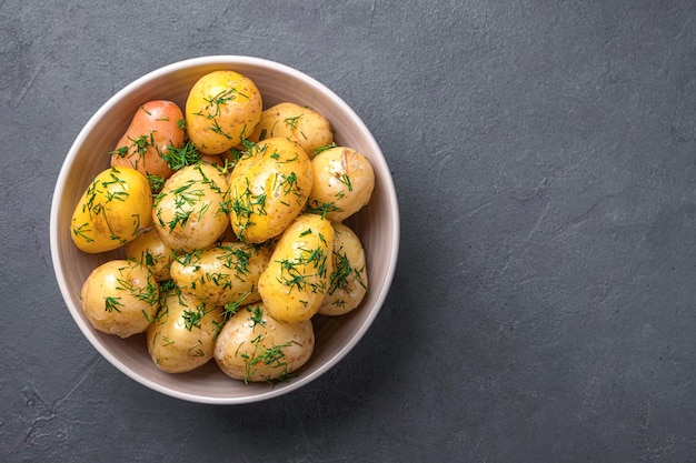 Pommes de terre bouillies non pelées avec aneth frais et huile sur fond graphite