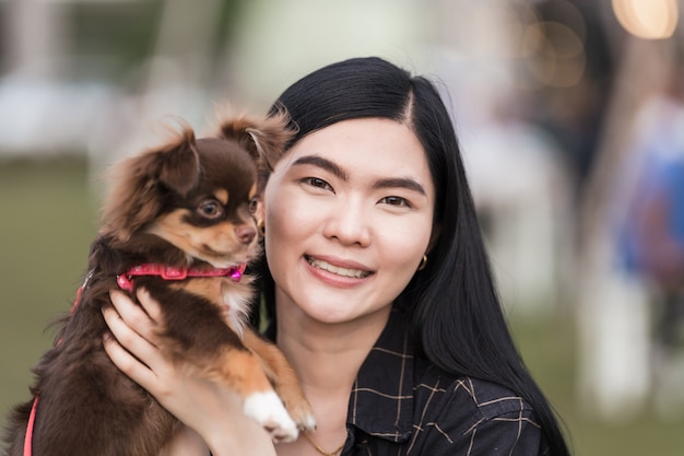 Photo portrait d'une belle fille jouant avec son adorable chiot à l'extérieur dans le parc public. un petit chien avec son propriétaire passe une journée au parc à jouer et à s'amuser. amour pour animaux de compagnie photo