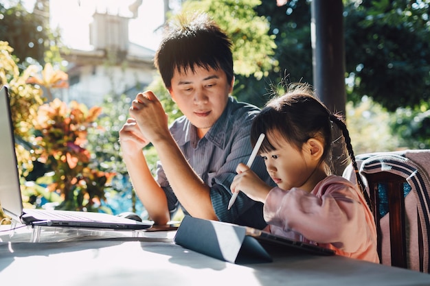 Portrait de famille du père et de la fille d'âge préscolaire utilisent un ordinateur pour étudier à la maison