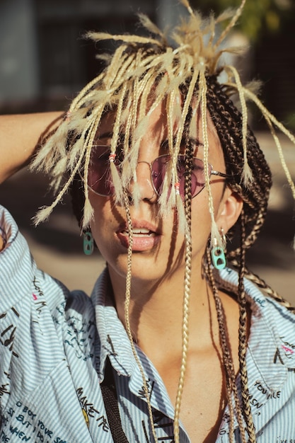 Photo portrait en gros plan d'une femme hipster élégante avec des lunettes de soleil roses de fantaisie et une coiffure à micro tresses