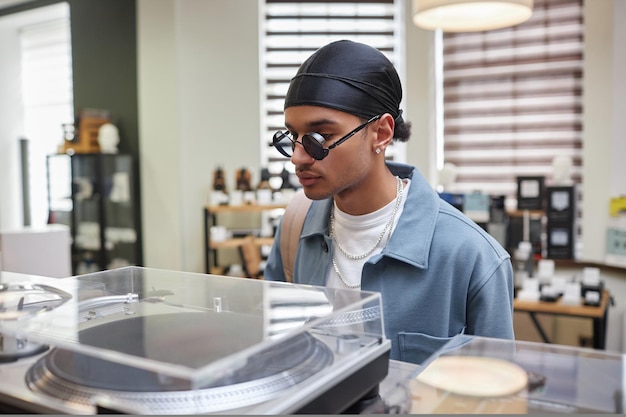 Photo portrait en gros plan d'un jeune homme noir élégant regardant un tourne-disque vinyle dans l'espace de copie du magasin de musique