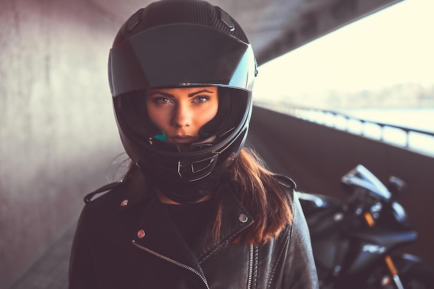 Portrait en gros plan d'une motarde portant une veste en cuir noire et un casque de sécurité à l'intérieur du pont.