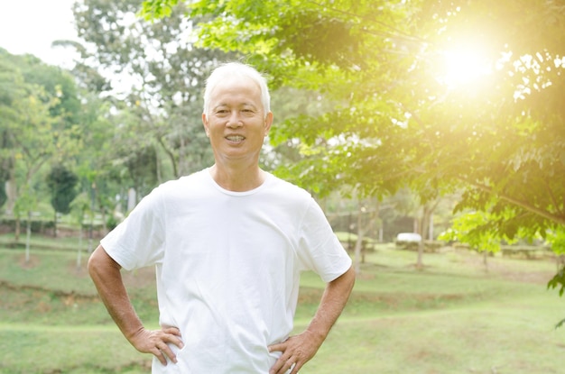 Photo portrait d'un homme âgé souriant avec la main sur la hanche debout contre les arbres dans le parc