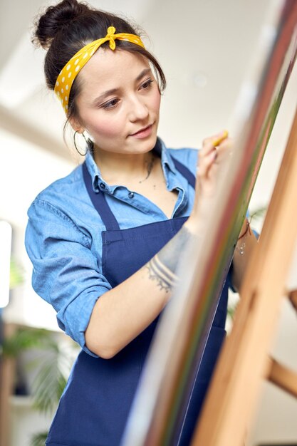 Photo portrait de jeune femme concentrée en tablier créant une peinture abstraite sur chevalet appliquant de la peinture