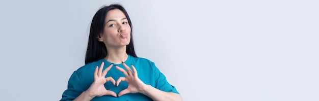 Portrait d'une jeune femme souriante montrant un geste cardiaque avec ses doigts isolés sur fond gris