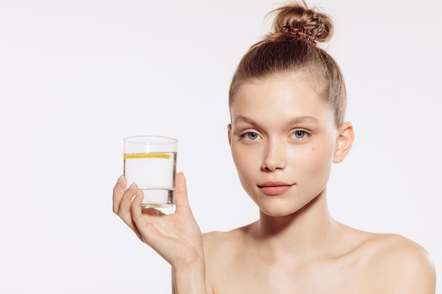 Portrait de jeune fille avec une belle peau parfaite tenant un verre d'eau avec du citron isolé sur fond de studio blanc