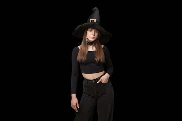 Portrait de jeune fille en chapeau de sorcière pointu et vêtements noirs est isolé sur fond noir Copie espace costume d'Halloween