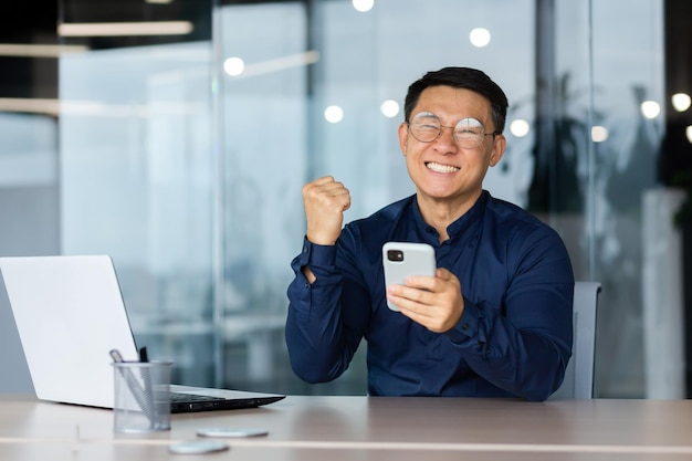 Photo portrait d'un jeune homme d'affaires heureux tenant un téléphone dans ses mains heureux montrant un geste oui