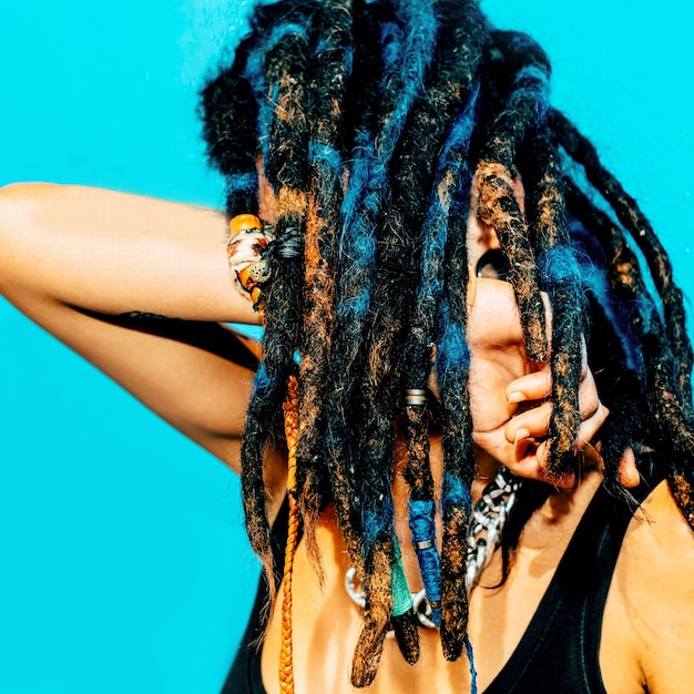 Photo rasta latino girl avec des dreadlocks, des piercings, des tatouages et élégante sur le mur bleu.