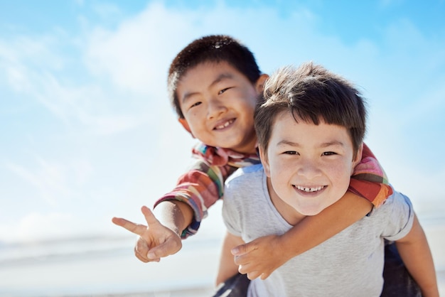 Photo signe de paix sur la plage et enfants asiatiques s'embrassent pendant les vacances de voyage au japon pour une liberté calme et une nature en plein air ciel bleu océan mer ou portrait de jeunesse heureux d'enfants amusants ou d'amis en vacances jouant sur le dos