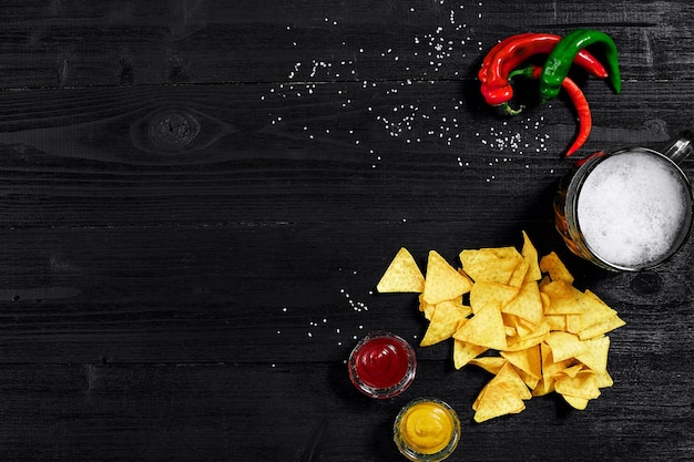 Snack pour chips de fête nachos avec sauces tomate ketchup moutarde et chope de bière sur fond noir...