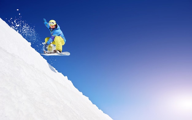 Snowboarder free rider sautant dans l'air en descente sur fond d'espace de copie de ciel bleu et de neige blanche