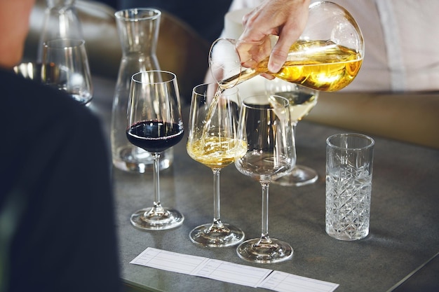 Photo sommelier versant du vin dans une carafe aux verres pendant l'entraînement aux boissons alcoolisées de près