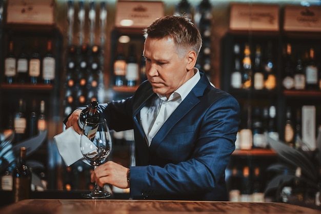 Photo un sommelier de vin élégant et soigné verse du vin rouge au verre pour le goûter.