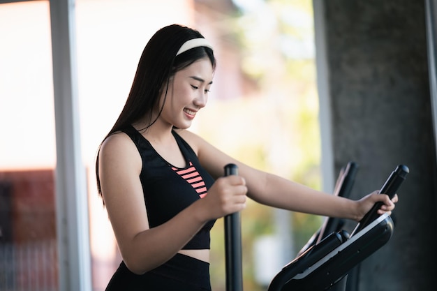 Photo sportive asiatique exerçant sur une machine elliptique dans la salle de gym la détermination de perdre du poids cardio fait son exercice sain concept de sport fitness femme machine elliptique