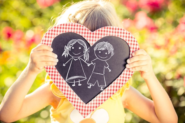 Photo tableau noir en forme de coeur avec des enfants dessinés dans les mains sur fond de fleur de printemps