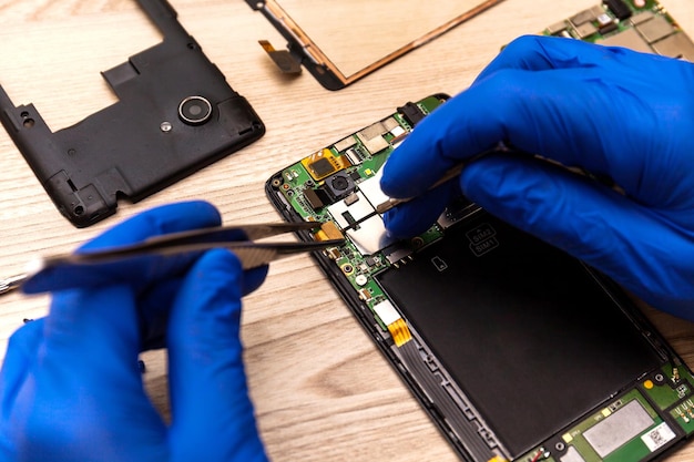 Le technicien réparant la carte mère du smartphone dans l'atelier sur la table