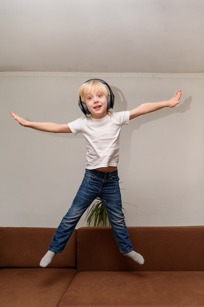 Photo teen boy, écouter de la musique sur les écouteurs et sauter sur le canapé.