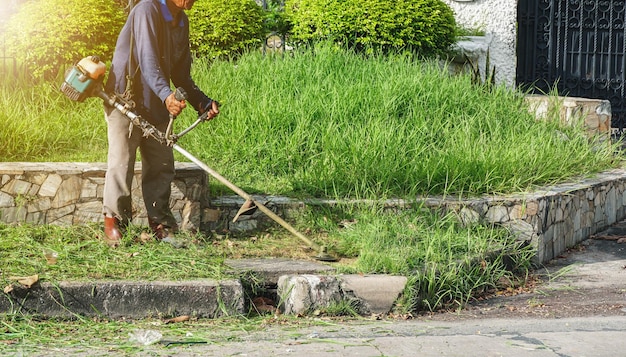 travailleur portant des vêtements de protection avec une tondeuse à essence dans ses mains, coupe de l'herbe en bordure de route.