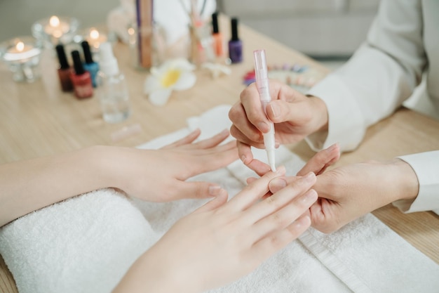 Photo travailleuse non reconnue dans le service à domicile tenant les mains d'une cliente appliquant de l'huile nourrissante sur les cuticules. esthéticienne faisant des travaux de manucure pour une cliente sur une table en bois. gros plan vie concept.