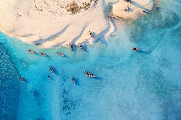 Photo vue aérienne des bateaux de pêche sur la côte de la mer tropicale avec plage de sable blanc au coucher du soleil. voyage d'été à zanzibar, en afrique. paysage avec bateaux, yachts, palmiers verts, eau bleu clair. vue de dessus