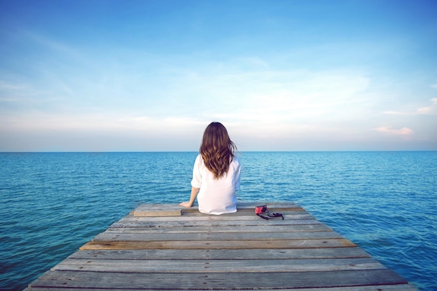 Vue arrière d'une femme assise sur une jetée au-dessus de la mer contre le ciel