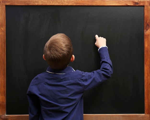 Photo vue arrière d'un garçon posant au tableau noir dans la salle de classe