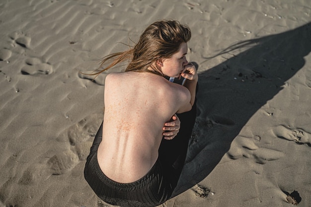 Photo vue à haut angle d'une femme sans chemise accroupi sur le sable