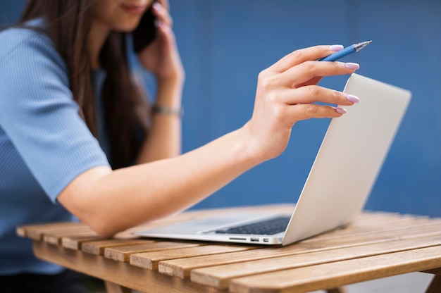 Vue latérale d'une femme défocalisée travaillant sur ordinateur portable tout en parlant sur smartphone