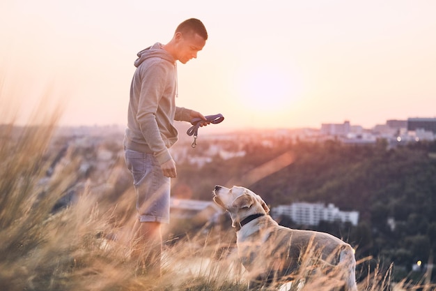 Photo vue latérale d'un homme avec un chien debout sur un champ contre le ciel au coucher du soleil