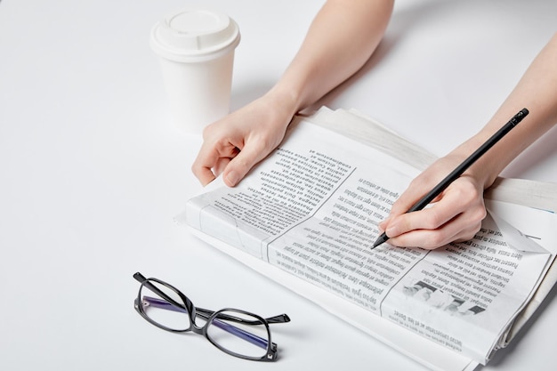 Photo vue recadrée d'une femme tenant un crayon près de verres à journaux et d'une tasse en papier sur blanc