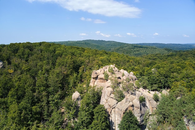 Aerial view of bright landscape with green forest trees and big rocky boulders between dense woods in summer Beautiful scenery of wild woodland