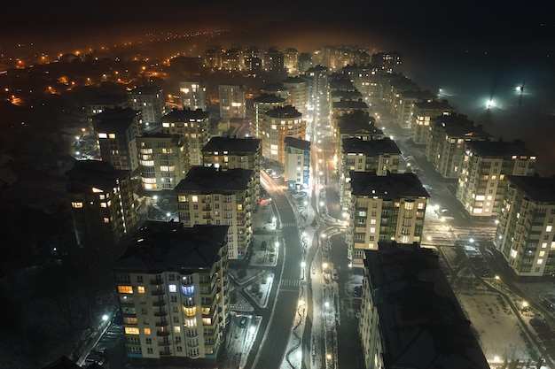 Aerial view of high rise apartment buildings and bright illuminated streets in city residential area at night Dark urban landscape