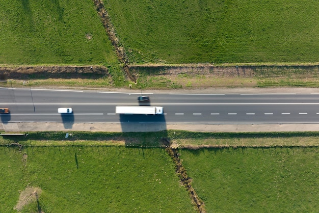 Aerial view of intercity road between green agricultural fields with fast driving cars Top view from drone of highway traffic