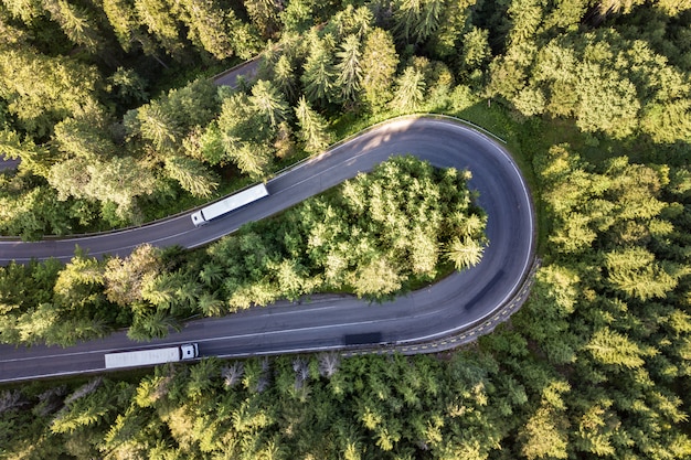 Aerial view of winding road in high mountain pass trough dense green pine woods.