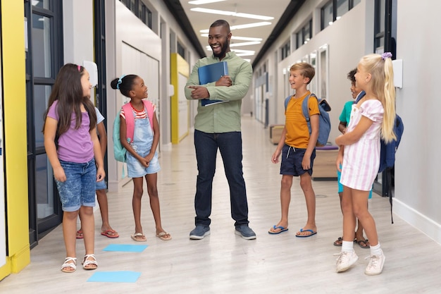 African american young male teacher talking to multiracial elementary students standing in corridor