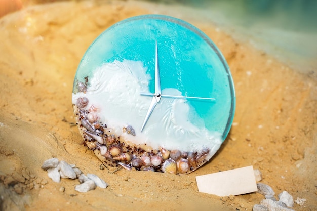 An alarm clock with seashells sitting on the sand with water vacation time Beach Time