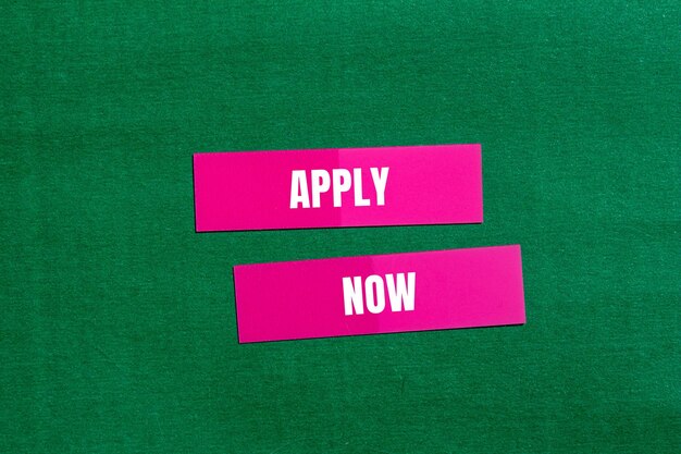 Photo apply now message written on pink paper with green background conceptual apply now symbol copy space