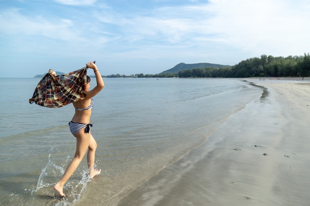 Asia teenage girls wearing bikini running at the beach by the sea background is a blue sky.