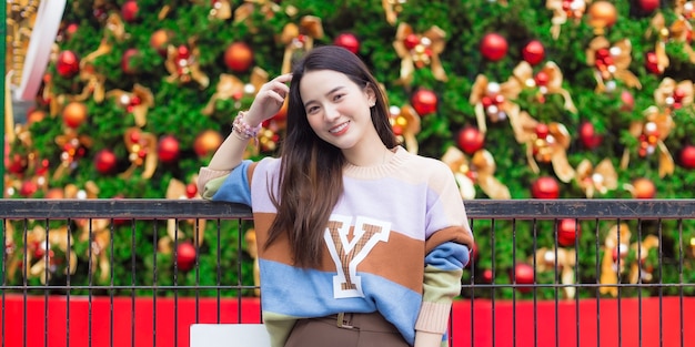 Photo asian beautiful girl wears colorful sweater and stands in front of christmas tree in new year celebrate theme.