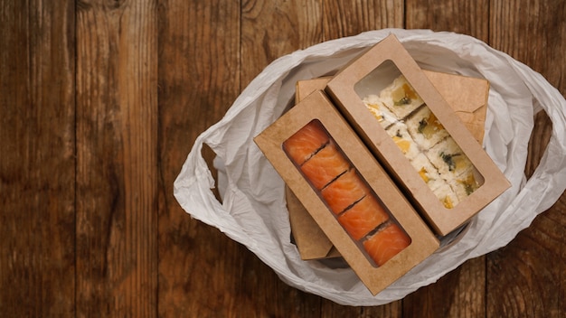 Photo asian food delivery. food in containers and in a package on a wooden background. japanese food and sushi packaging.