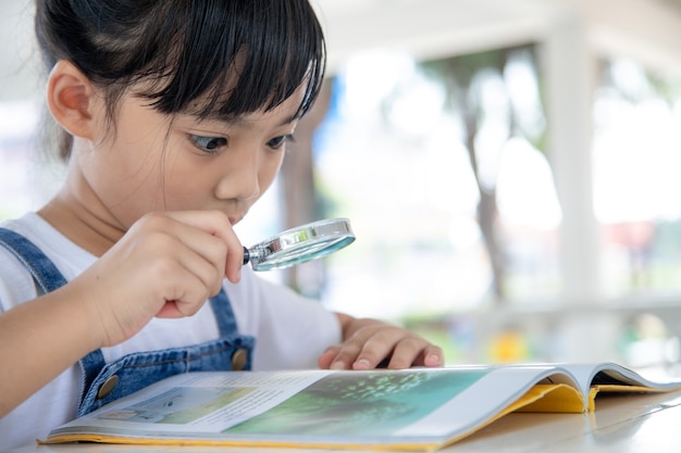 Photo asian little girl reading the books on the desk with a magnifying glass