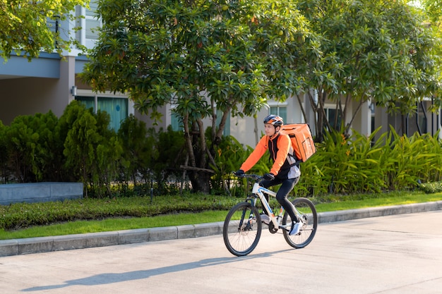 Asian man courier on bicycle delivering food in town streets with a hot food delivery from take aways and restaurants to home, express food delivery and shopping online concept.