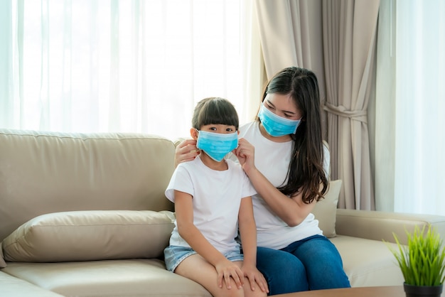 Photo asian mother wearing wearing to her daughter healthy face mask sitting