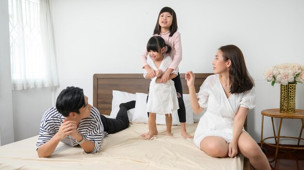 Photo asian parents with two little daughters jumping on the bed in bedroom happy family concept